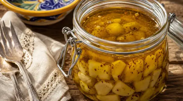 Un barattolo di aglio sott'olio, pronto per essere usato in ogni ricetta. Accanto, una forchetta e un tovagliolo ricamato.