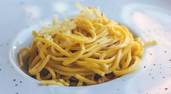 Maccheroni alla chitarra molisani, un piatto di pasta fresca condita con formaggio grattugiato e pepe nero, serviti in un piatto bianco.