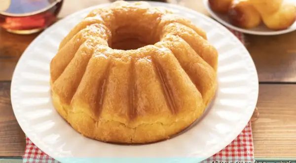 Un soffice babà, pronto per essere inzuppato, evoca la **babà ricetta originale**. Accanto, un bicchierino di rum e altri babà in miniatura.