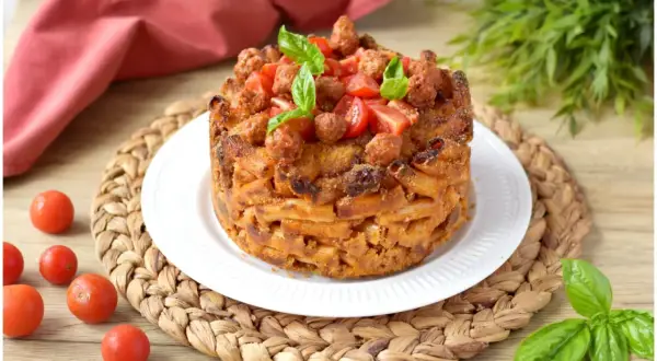 Un invitante pasta timbale, dorato e ripieno, guarnito con pomodorini e basilico fresco.
