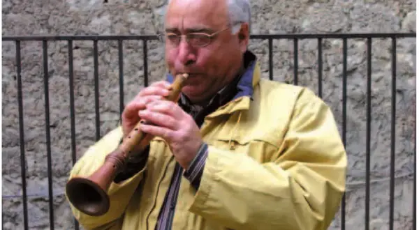 Uomo con occhiali suona uno strumento a fiato, una piva, con un suono melodioso.