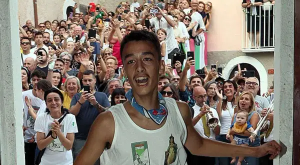 Giovane festante con la maglia "Madonna di Loreto" a Pacentro, tra una folla che filma e applaude.