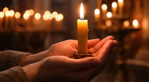 Mani che sorreggono una candela accesa, un momento di pace quando si accende la candela della candelora, con altre luci soffuse sullo sfondo.