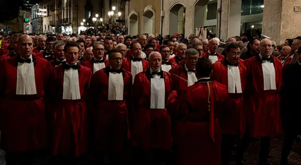 Uomini in toga rossa partecipano alla processione del Venerdì Santo a Sulmona, un momento di profonda spiritualità e tradizione.