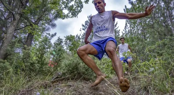 Due giovani atleti corrono a piedi nudi nel bosco, partecipando alla "Corsa degli Zingari". Il primo è in primo piano, in pieno balzo.