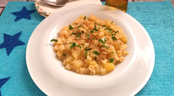 Un piatto di pasta e patate con provola filante, guarnito con prezzemolo fresco e un pizzico di peperoncino.
