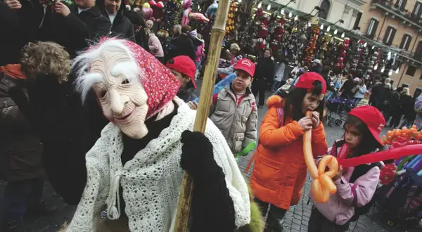 Una maschera della Befana saluta la folla, mentre i bambini giocano con palloncini gonfiabili. Si festeggia la Befana!