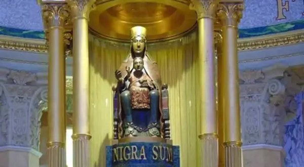 Statua dorata di una Maria nera con Gesù Bambino, su un piedistallo con iscrizione latina.