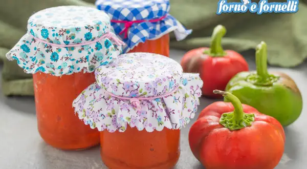 Barattoli di conserva di peperoni napoletana con tappi decorati, circondati da peperoni freschi rossi e verdi.