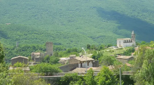Il gigante di acciaio veglia su un borgo antico, tra torri e case di pietra, sotto un monte verdeggiante.