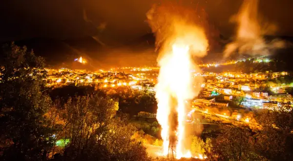 Un imponente falò illumina la notte, celebrando le glorie di San Martino. Le fiamme danzano sopra un villaggio illuminato, creando uno spettacolo magico.