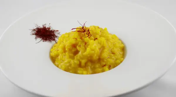 Un cremoso risotto alla milanese, giallo intenso, guarnito con pistilli di zafferano e accompagnato da una piccola porzione di zafferano essiccato.