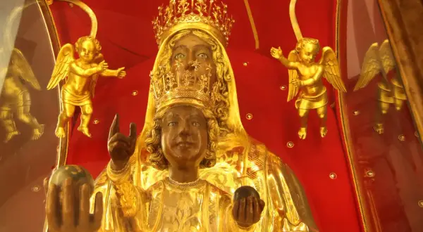 Statua della Madonna Nera, con il Bambino Gesù, circondata da angeli dorati su sfondo rosso.