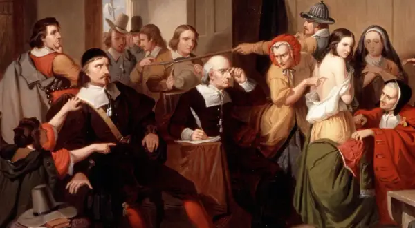 Un gruppo di persone esamina una giovane donna, cercando segni fisici delle streghe. Un uomo scrive, mentre altri osservano con sospetto.