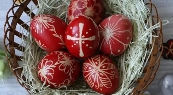Uova di Pasqua rosse decorate con motivi floreali e una croce, simbolo uovo di Pasqua significato di rinascita e speranza, in un cesto.