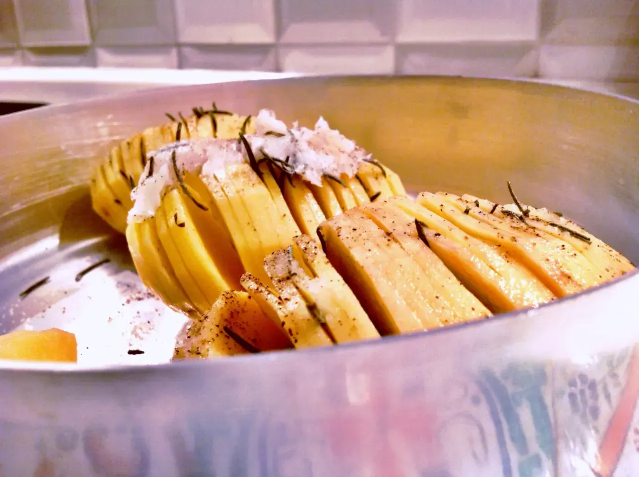 Patate al coppo, tagliate a fisarmonica e condite con erbe aromatiche, pronte per essere cotte.