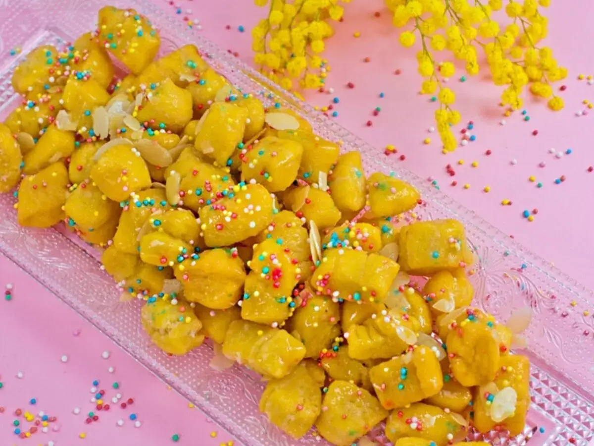 Dolcezza dorata: la ricetta cicerchiata marchigiana, decorata con confettini colorati e mandorle, pronta per essere gustata.
