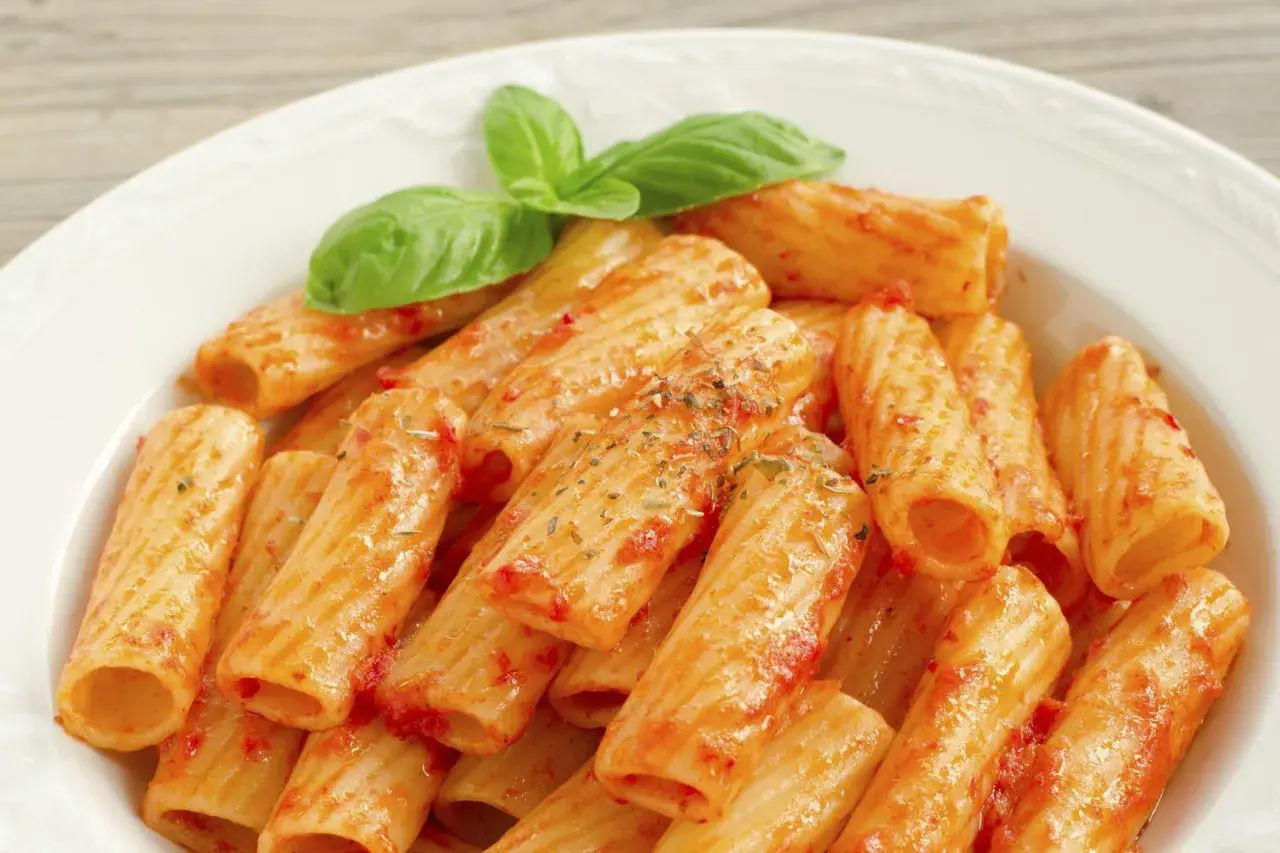 Un piatto di rigatoni al sugo, conditi con erbe aromatiche e guarniti con foglie di basilico fresco. Il maccarone, nella sua semplicità, racchiude un significato di convivialità e tradizione.