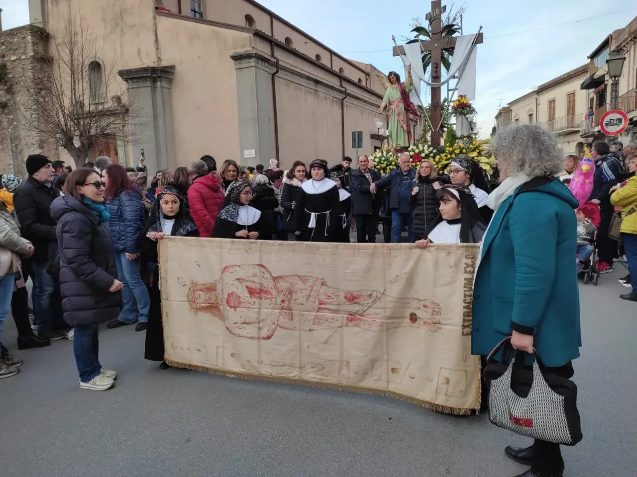 Processione con il telo della Veronica, raffigurante Cristo, tra la folla e una statua lignea.