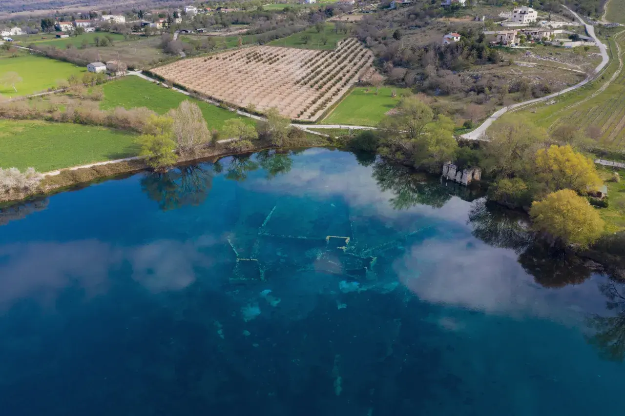 Le rovine sommerse nel lago azzurro evocano un'Atlantide d'Abruzzo. Campi verdi e alberi circondano questo luogo magico.