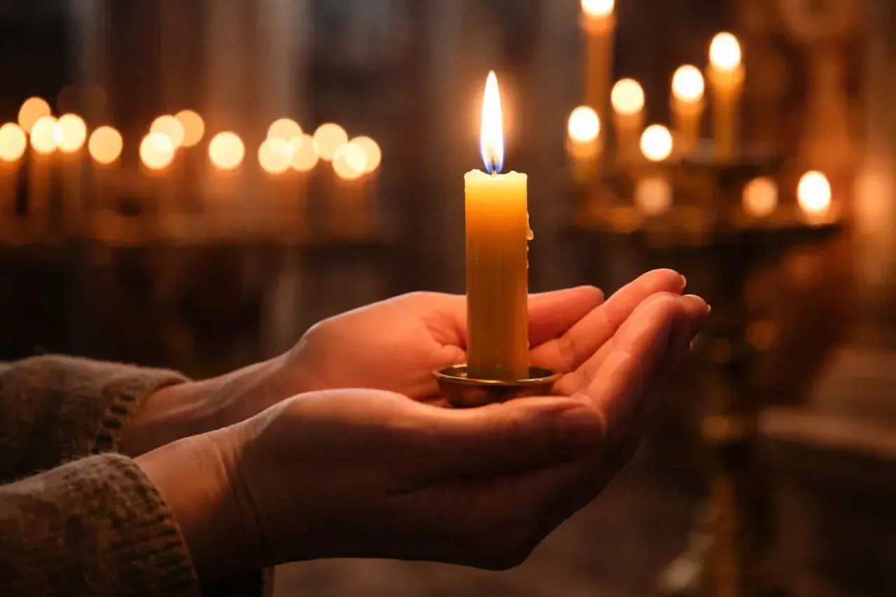 Mani che sorreggono una candela accesa, un momento di pace quando si accende la candela della candelora, con altre luci soffuse sullo sfondo.