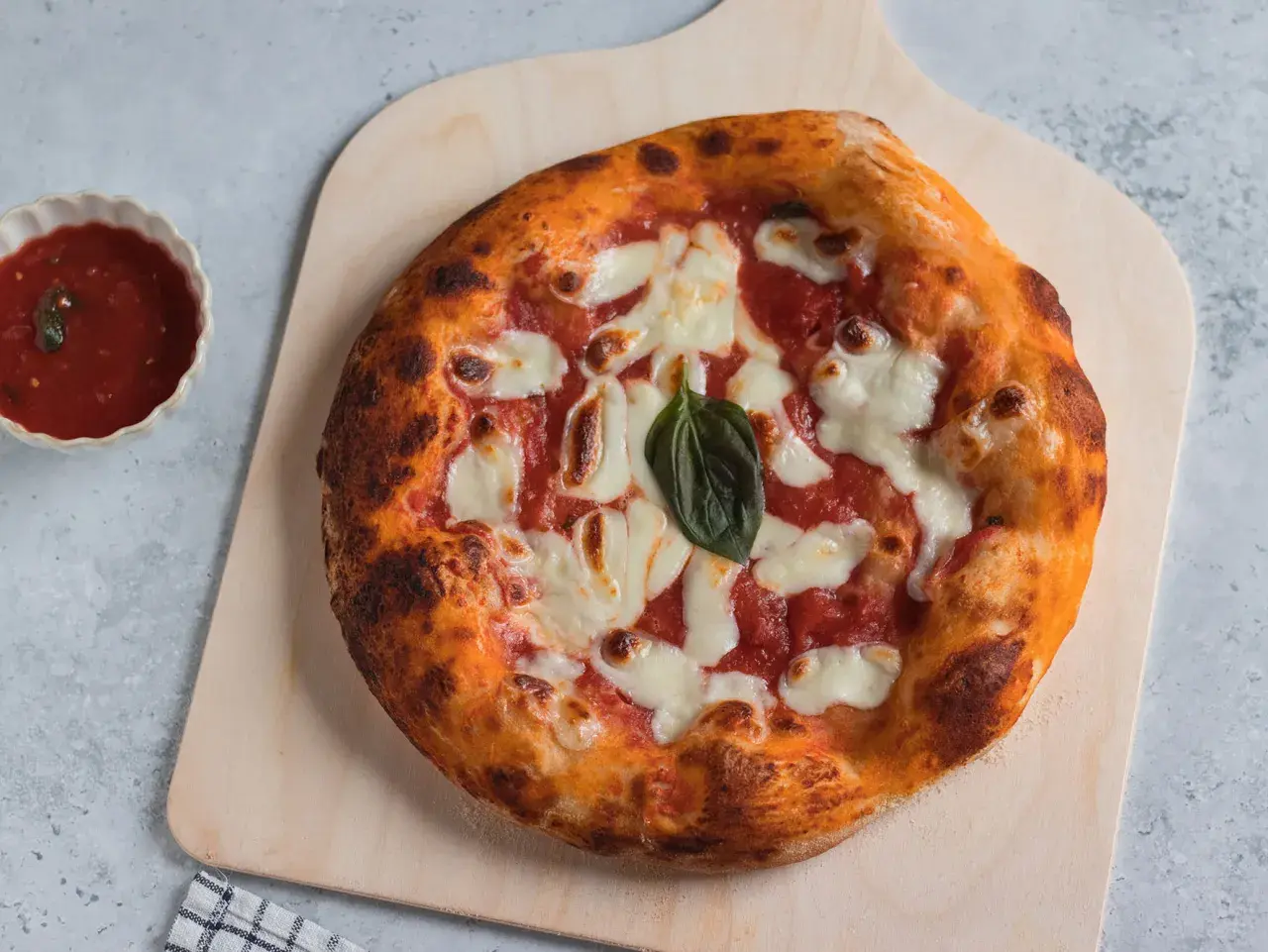 Pizza margherita appena sfornata, con crosta dorata e mozzarella filante. Accanto, una ciotolina di salsa di pomodoro, perfetta per chi ama la pizzelle ricetta tradizionale.