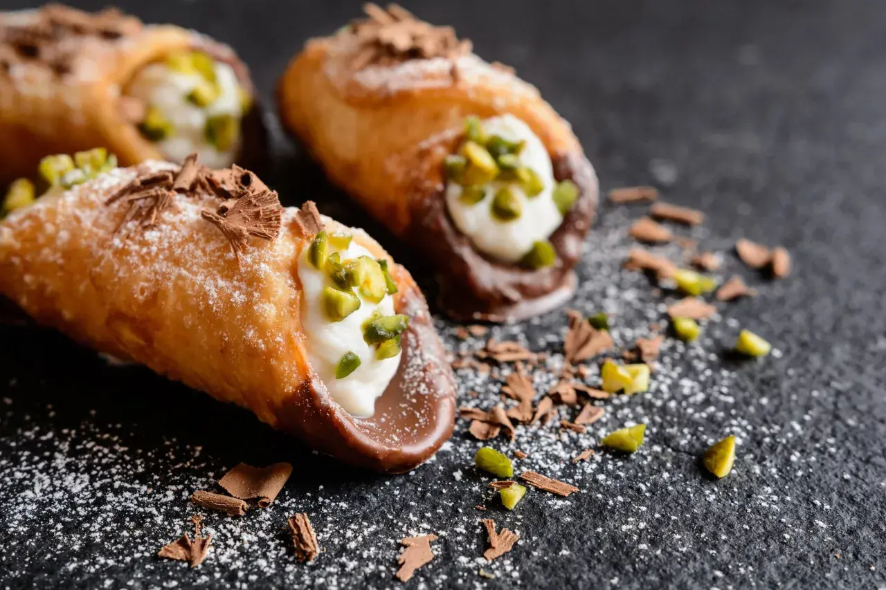 Cannoli siciliani ricetta della nonna: croccanti cialde ripiene di crema, guarnite con pistacchi e scaglie di cioccolato.