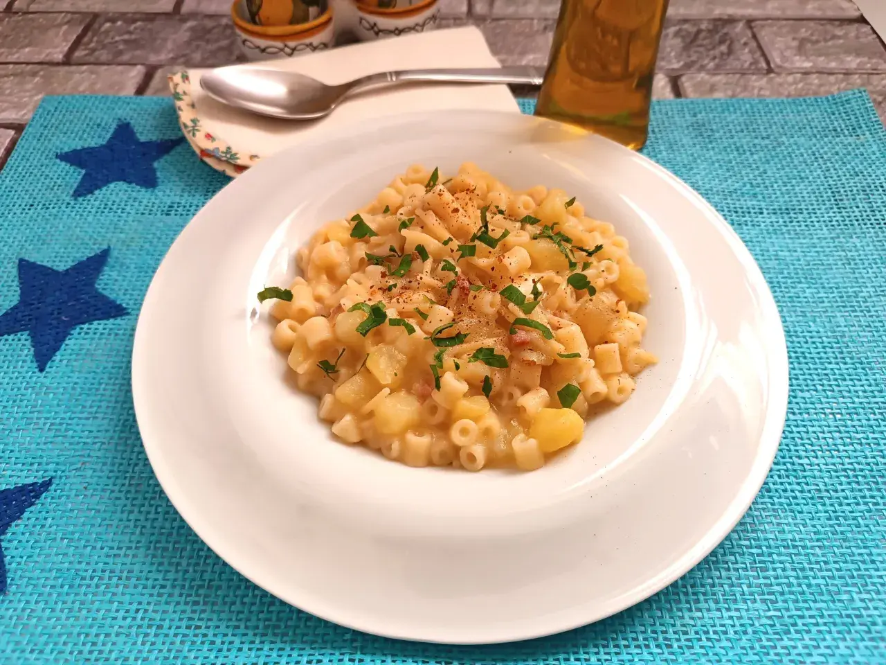 Un piatto di pasta e patate con provola filante, guarnito con prezzemolo fresco e un pizzico di peperoncino.