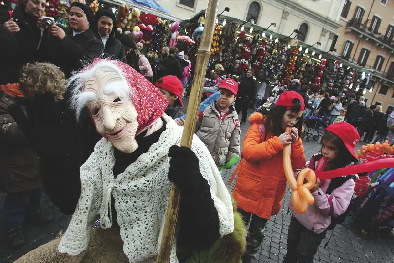 Una maschera della Befana saluta la folla, mentre i bambini giocano con palloncini gonfiabili. Si festeggia la Befana!