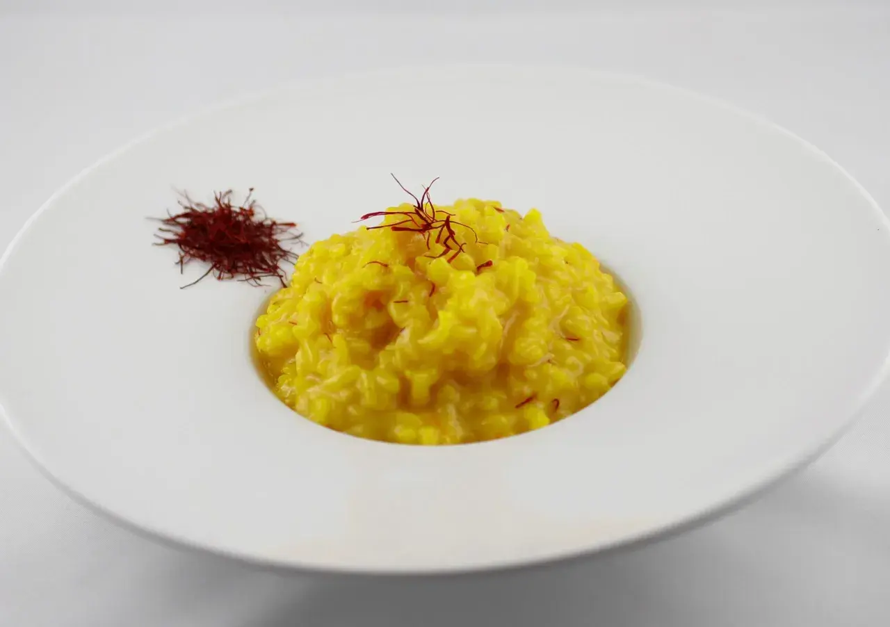 Un cremoso risotto alla milanese, giallo intenso, guarnito con pistilli di zafferano e accompagnato da una piccola porzione di zafferano essiccato.