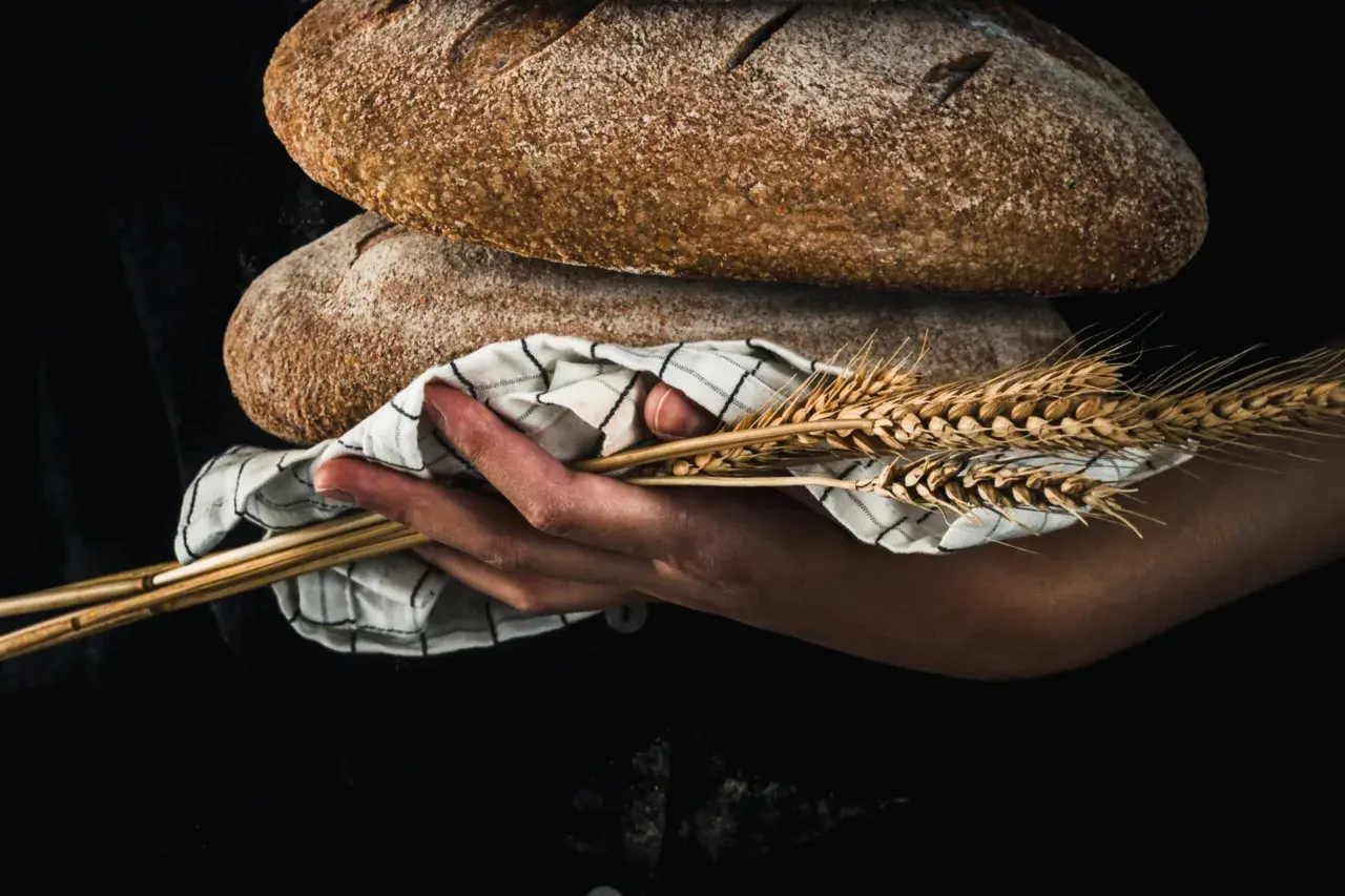 Mani che sorreggono pani rustici e spighe di grano, evocando il significato pagano del raccolto e della fertilità.