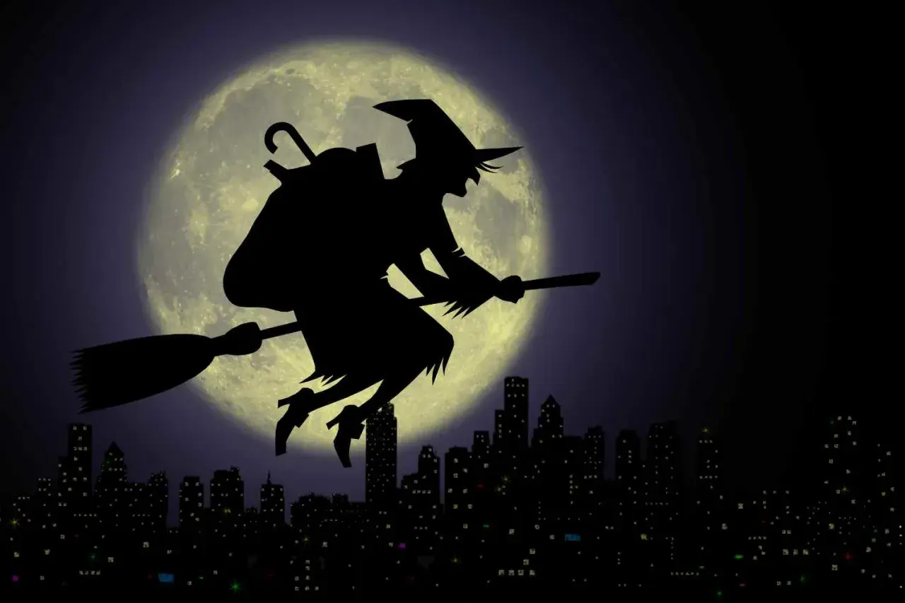 La Befana vola su una scopa contro la luna piena, sopra una città illuminata. Viva viva la Befana!