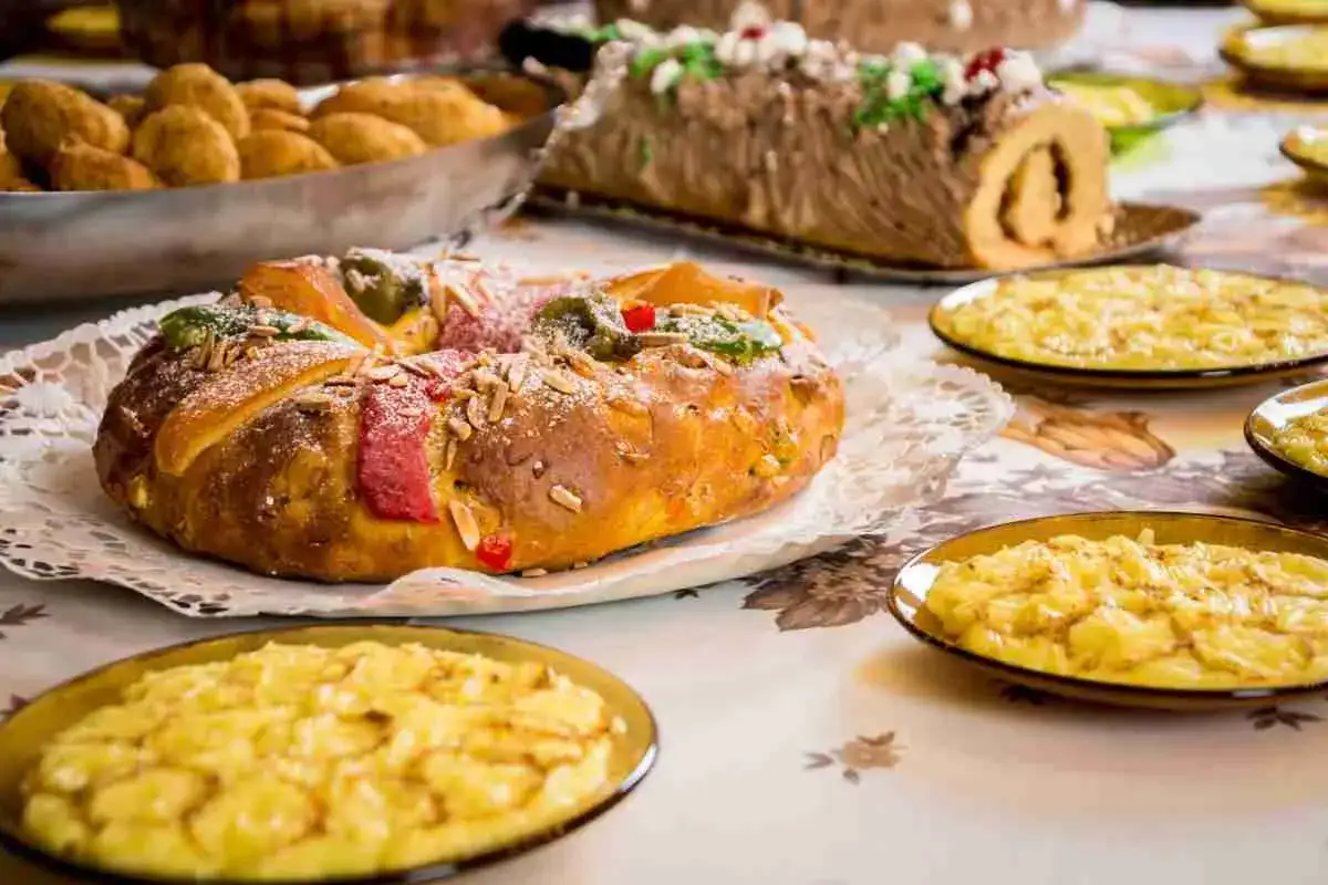 Dolce tipico dell'Epifania: un Roscón de Reyes decorato con frutta candita e mandorle, accompagnato da dolcetti.