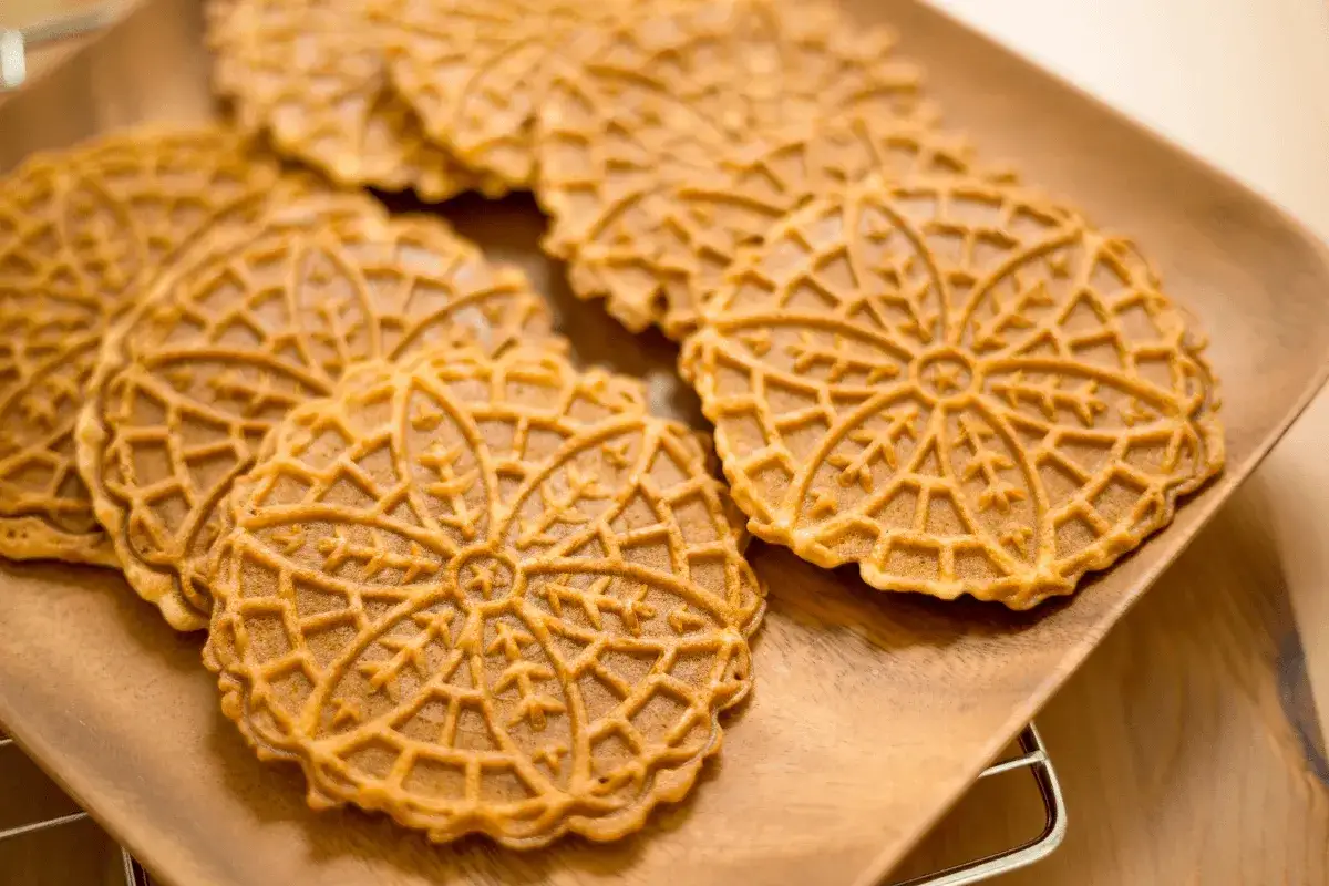 Pizzelle ricetta: biscotti dorati con decorazioni a fiore su un piatto di legno.