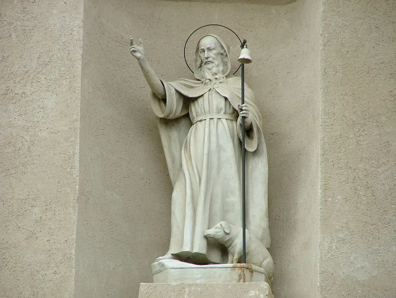 Statua di Sant'Antonio Abate con cane, bastone e campana, che evoca la sua leggenda.
