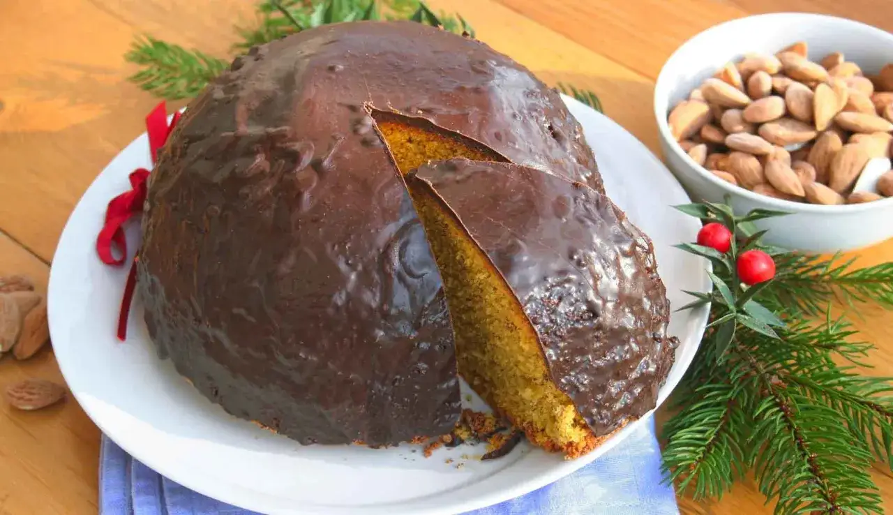 Parrozzo abruzzese ricoperto di cioccolato fondente, con una fetta tagliata. Accanto, mandorle e decorazioni natalizie.