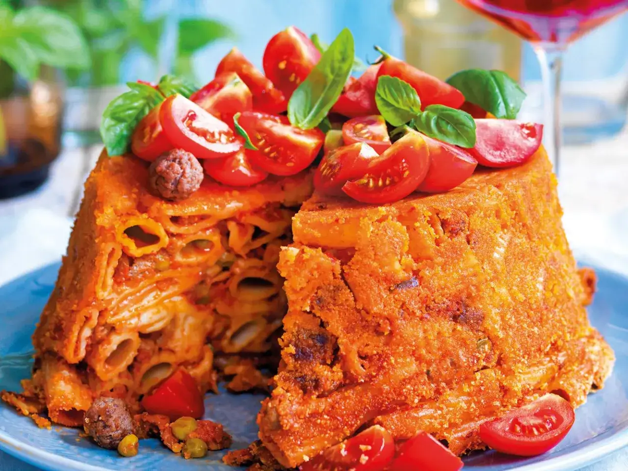 Un invitante pasta timbale, ricco di rigatoni, sugo e polpettine, guarnito con pomodorini freschi e basilico.