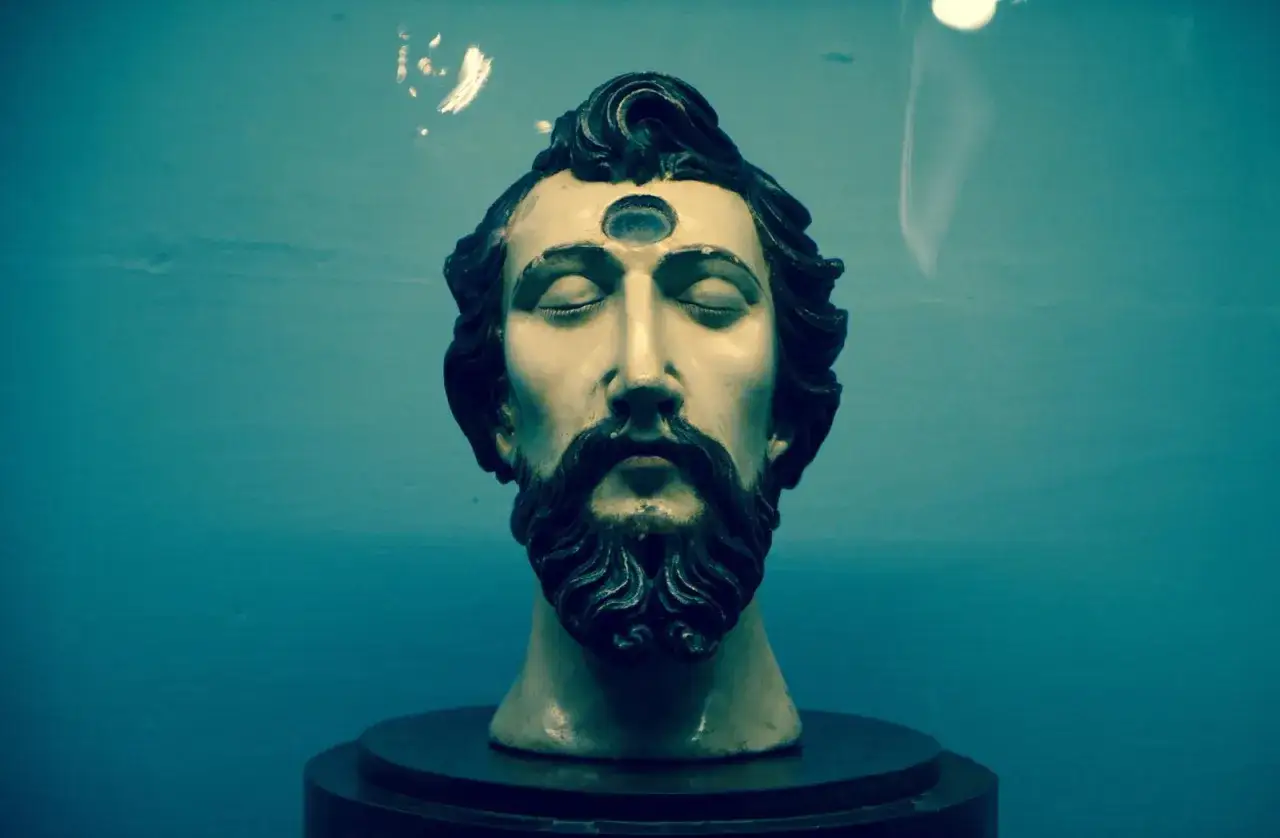 Busto di Cristo Acheropita con terzo occhio, occhi chiusi e barba fluente, su sfondo blu.