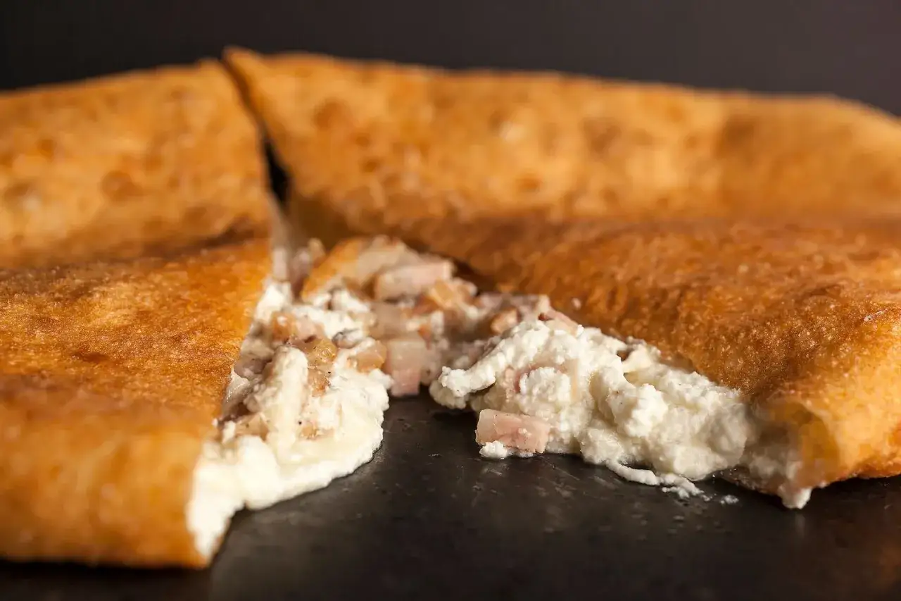 Pizza fritta napoletana: impasto dorato e ripieno cremoso di ricotta e ciccioli. Ingredienti semplici per un sapore unico.