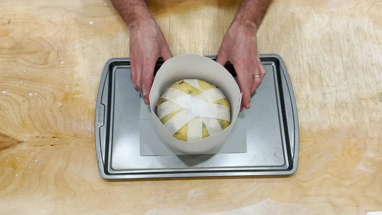 Mani che preparano un panettone natalizio, avvolto in carta e pronto per la cottura su una teglia.