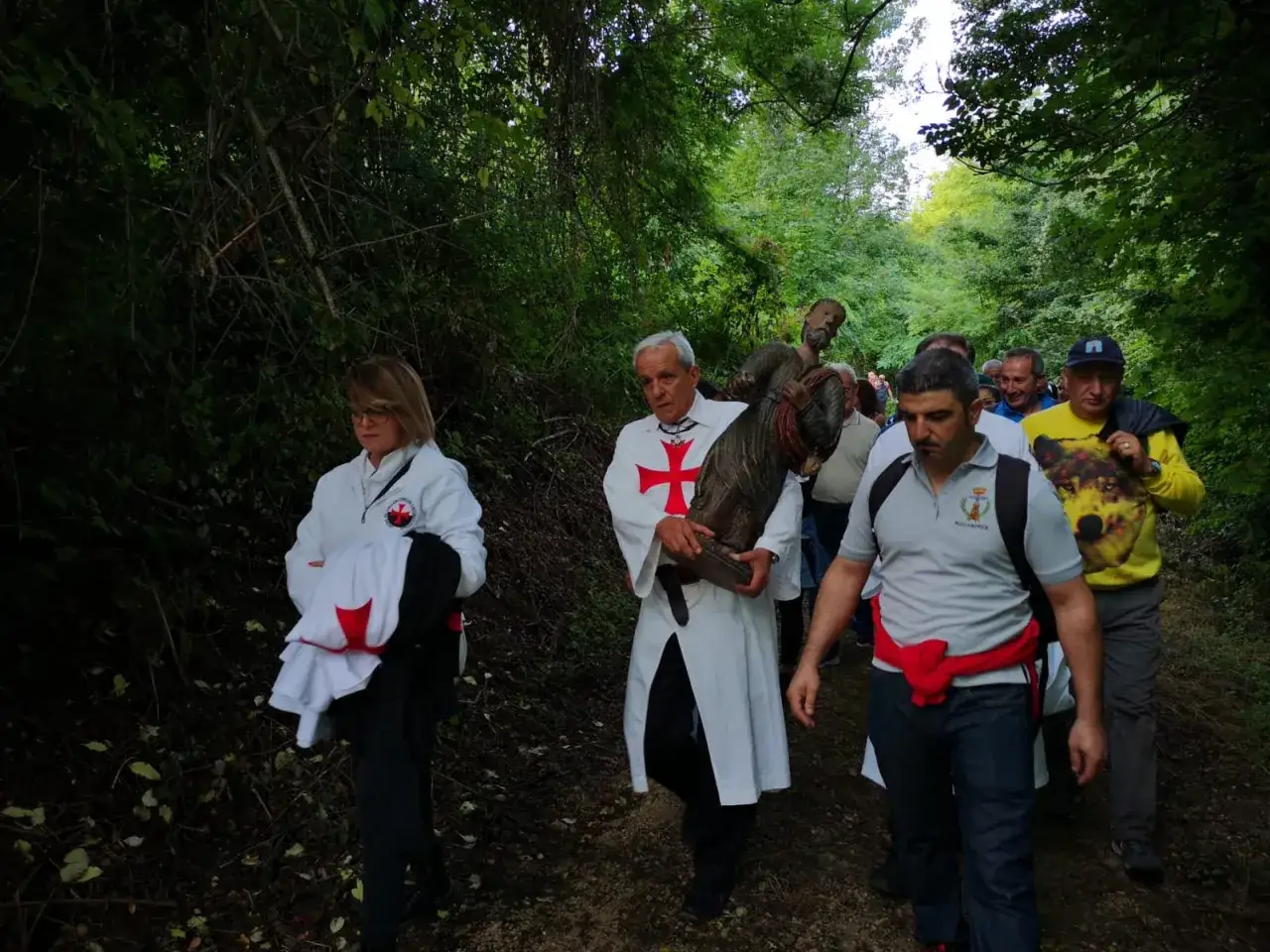 Processione con statua di San Bartolomeo in legio, tra alberi e fedeli.