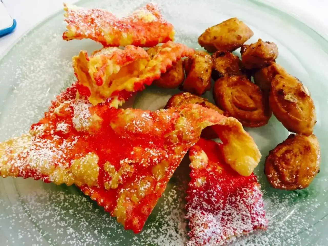 Dolci fritti, alcuni rossi e croccanti, altri dorati e a spirale, cosparsi di zucchero a velo. Un assaggio della ricetta cicerchiata marchigiana.