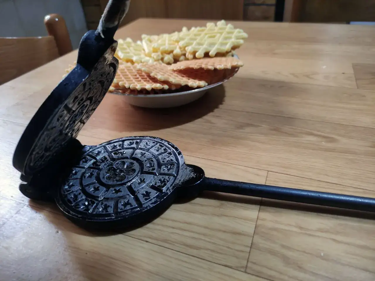 Vecchia piastra per pizzella abruzzese con dolci appena sfornati su un tavolo di legno.