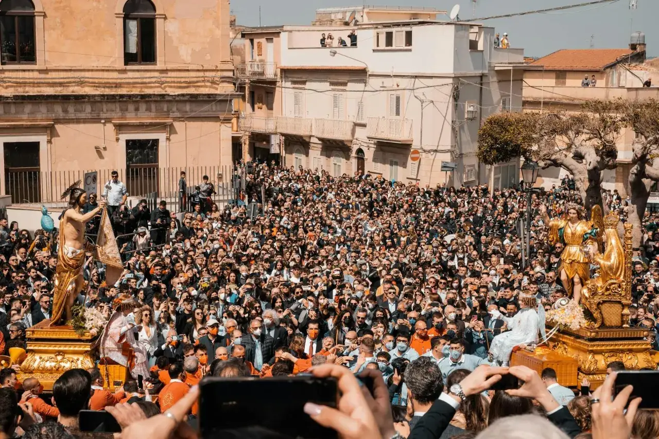Una folla immensa partecipa ai riti pasquali, documentando con i cellulari la processione di statue dorate per le strade di una città.