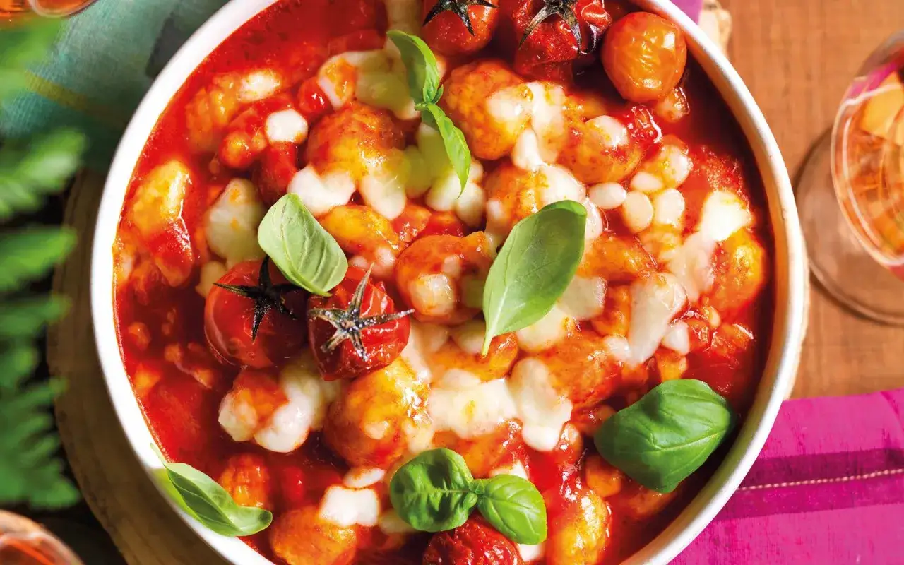 Gnocchi alla napoletana fumanti, con pomodorini e mozzarella filante, guarniti da foglie di basilico fresco.
