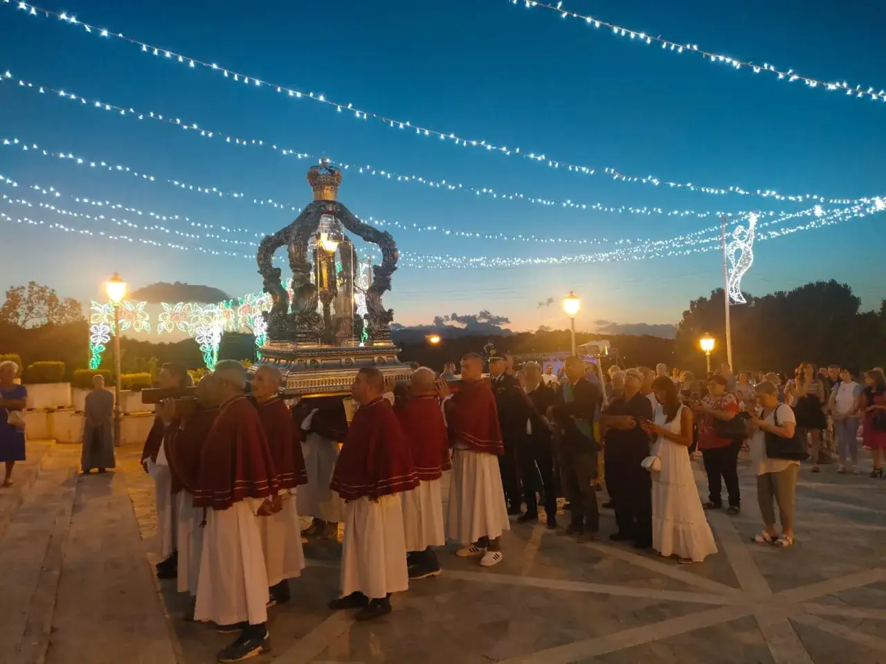 Processione serale con un carro decorato, forse con un velo di Gesù, illuminato da luci.
