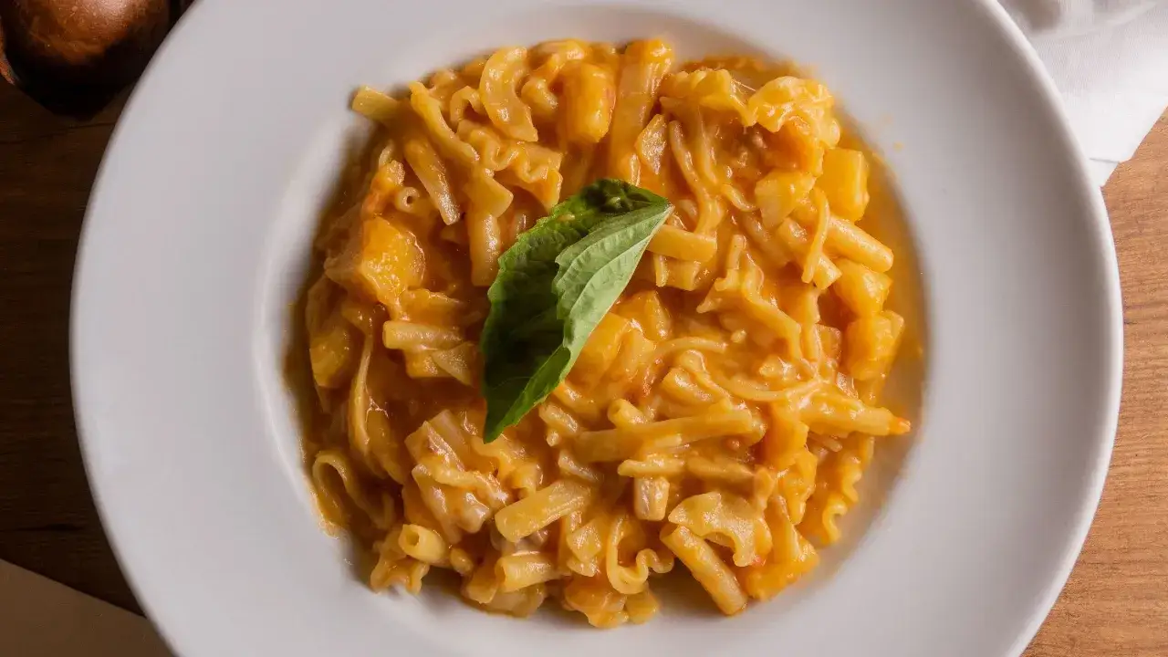 Piatto di pasta e patate con provola filante, guarnito con una foglia di basilico fresco.