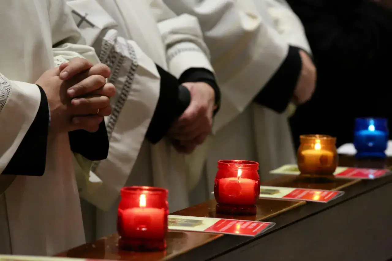 Mani giunte in preghiera, mentre si accende la candela della candelora. Fiammelle rosse e arancioni illuminano la cerimonia.