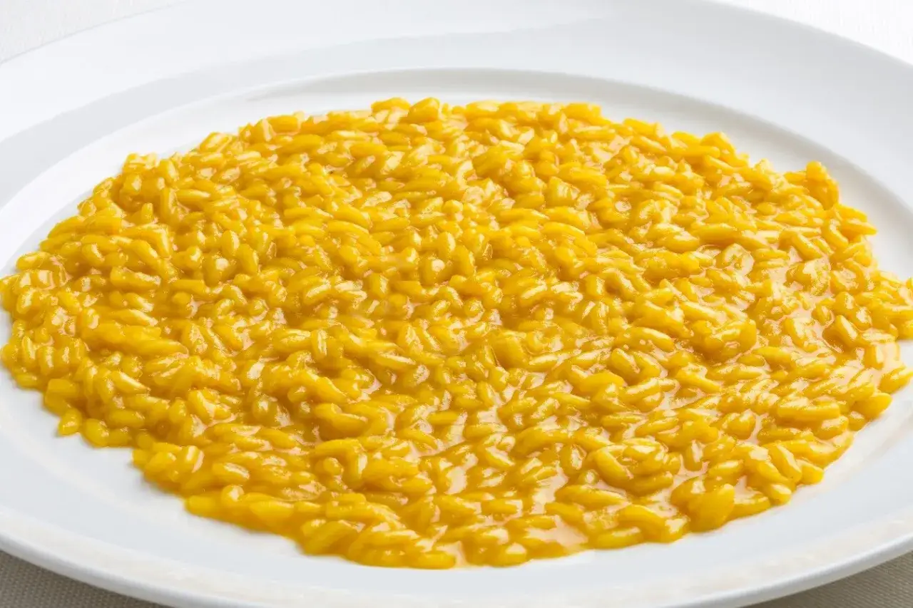 Un cremoso risotto alla milanese, dal colore giallo intenso, servito su un piatto bianco.