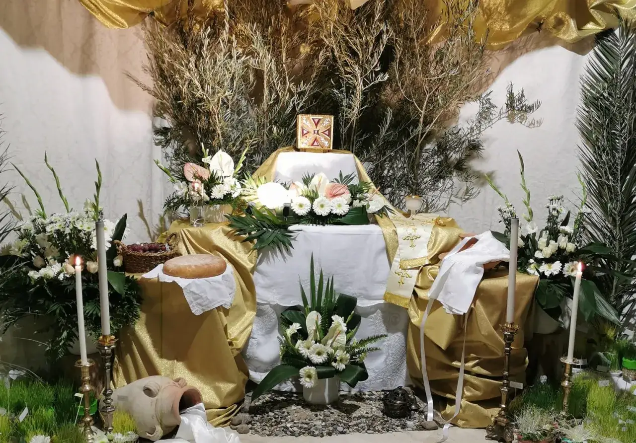 Altare addobbato per il giro dei sepolcri: pane, uva, candele, fiori bianchi e oro, con un ostensorio al centro.